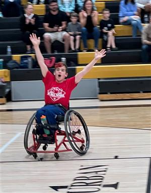 a student in a wheelchair with his arms raised