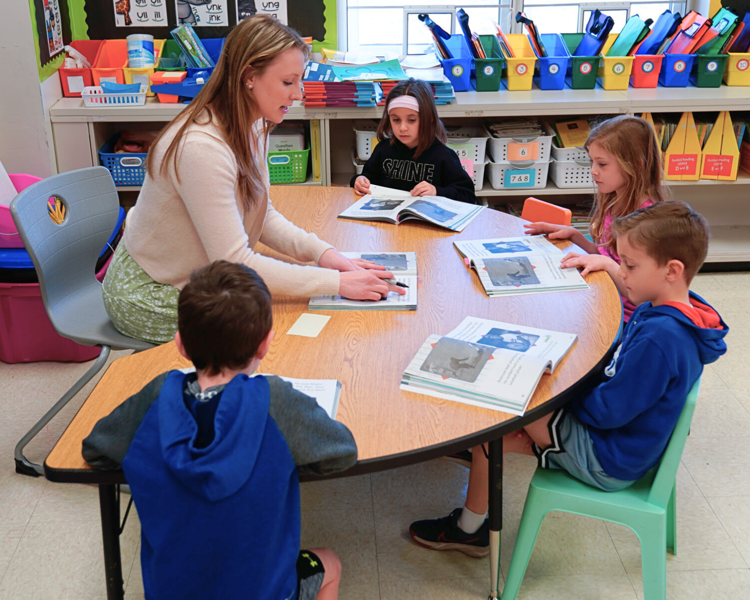 A high school student helps instruct four elementary students in reading.