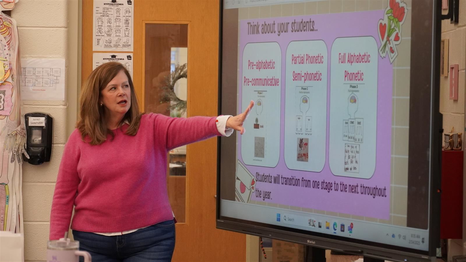 A teacher instructs a class in front of a screen